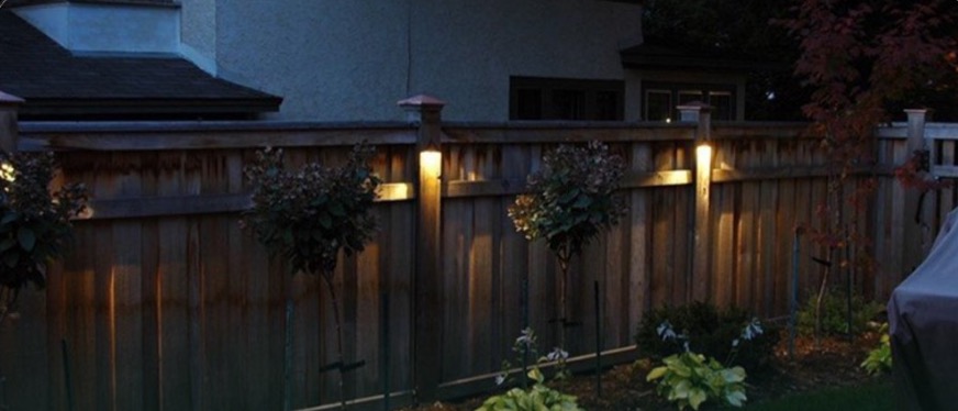 Solar post lights glowing on a fence at dusk